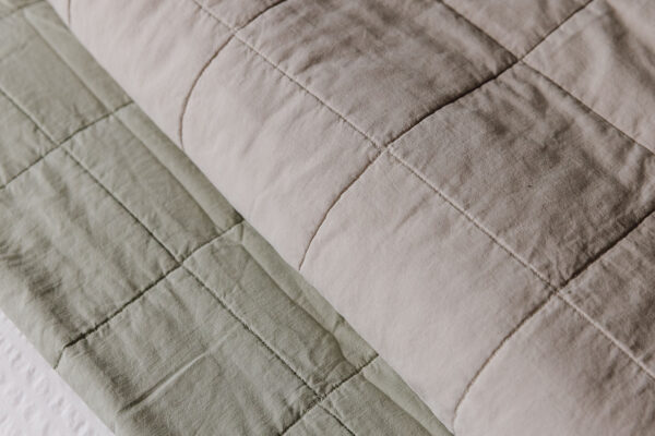 Stonewash quilted bedspreads in muted sage and greige. Cropped, closeup view.