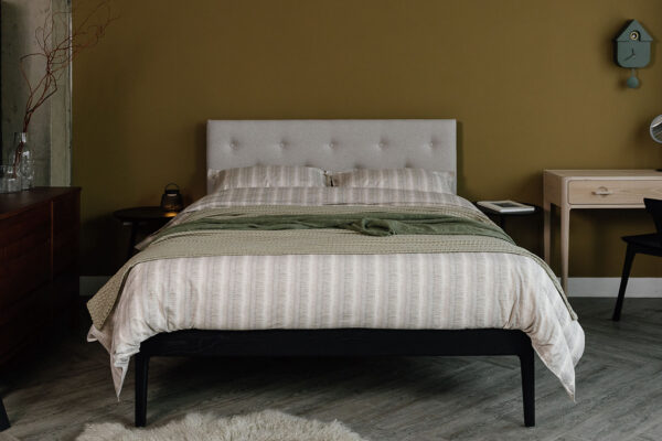 Black Oak Bloomsbury upholstered with Amatheon Porcelain. Dressed with a cotton duvet set with a fine dash stripe pattern, and loose green throws.
