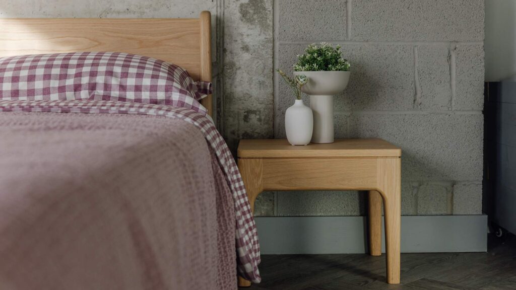 Original Oak Camden table with vases, placed next to an oak Pimlico bed with purple gingham bedding and matching bedspread.