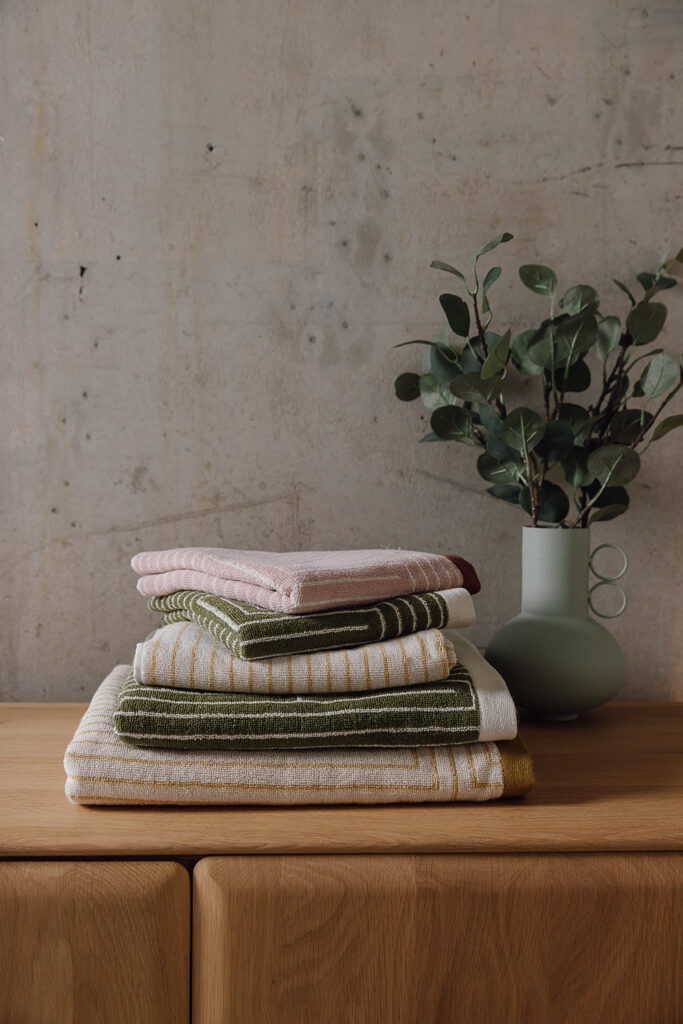 Stack of grid pattern towels. From top to bottom: pink hand towel, green hand towel, yellow hand towel, green bath towel, yellow bath sheet.