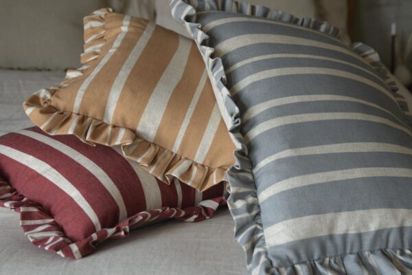 3 Cushions with ruffled edges stacked on a bed. One red, one mustard, one blue.