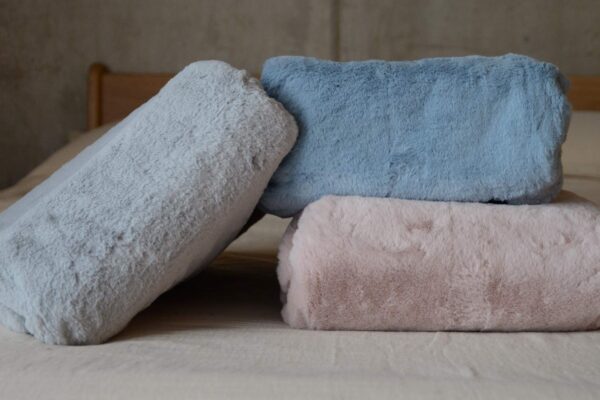 3 folded faux fur throws on a bed. Blue, grey and pink.