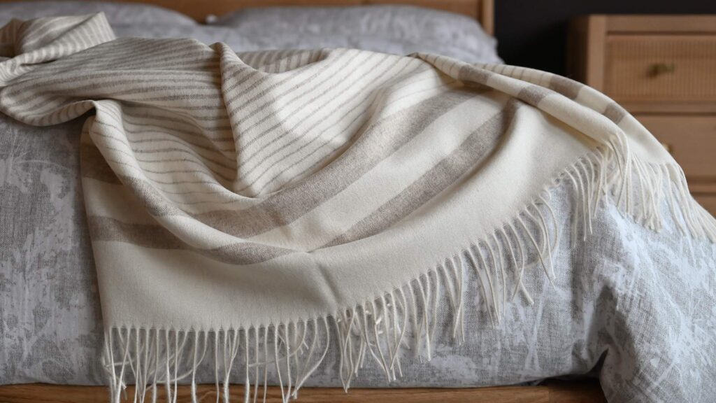 A warm, light brown and cream striped woollen throw with fringe detail.