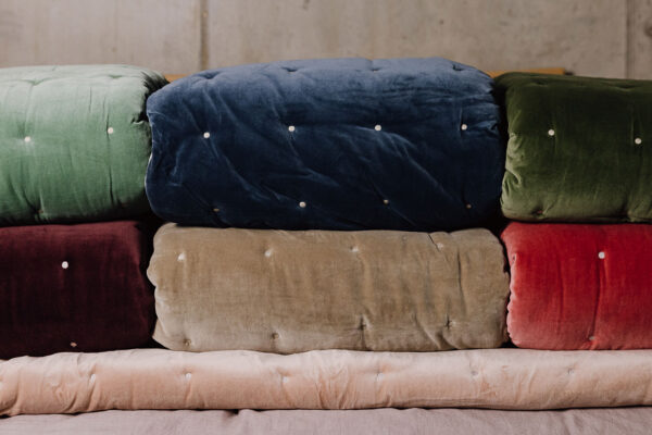 Stack of velvet reversible quilted throws in various colours.