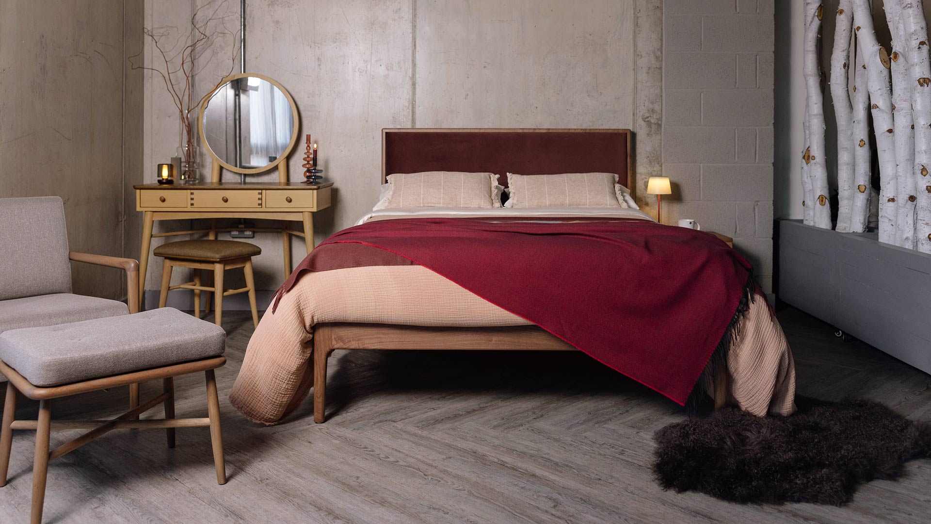 Walnut Carlisle bed frame with dark red headboard with red ben linens. Dressing table, a grey chair and stool and a dark faux fur rug also in the photograph.