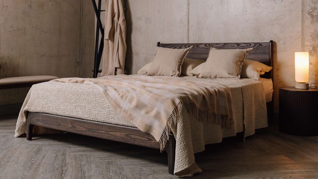 Cool Smoked Ash Carnaby bed base with neutral bedding including an ecru waffle bedspread, beige linen cushions and a checkered wool throw.